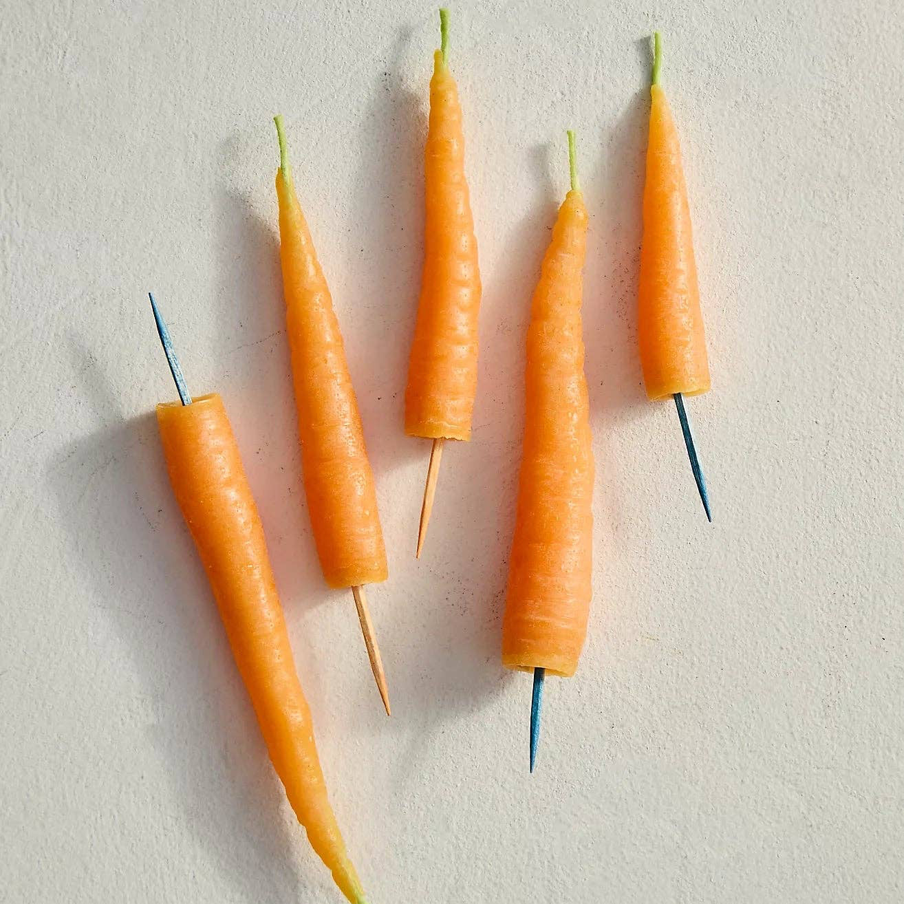 Five small carrots with green tops arranged on a light gray background