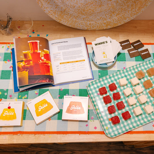 Table with a cookbook, candy, and a checkered placemat on a checkered tablecloth.