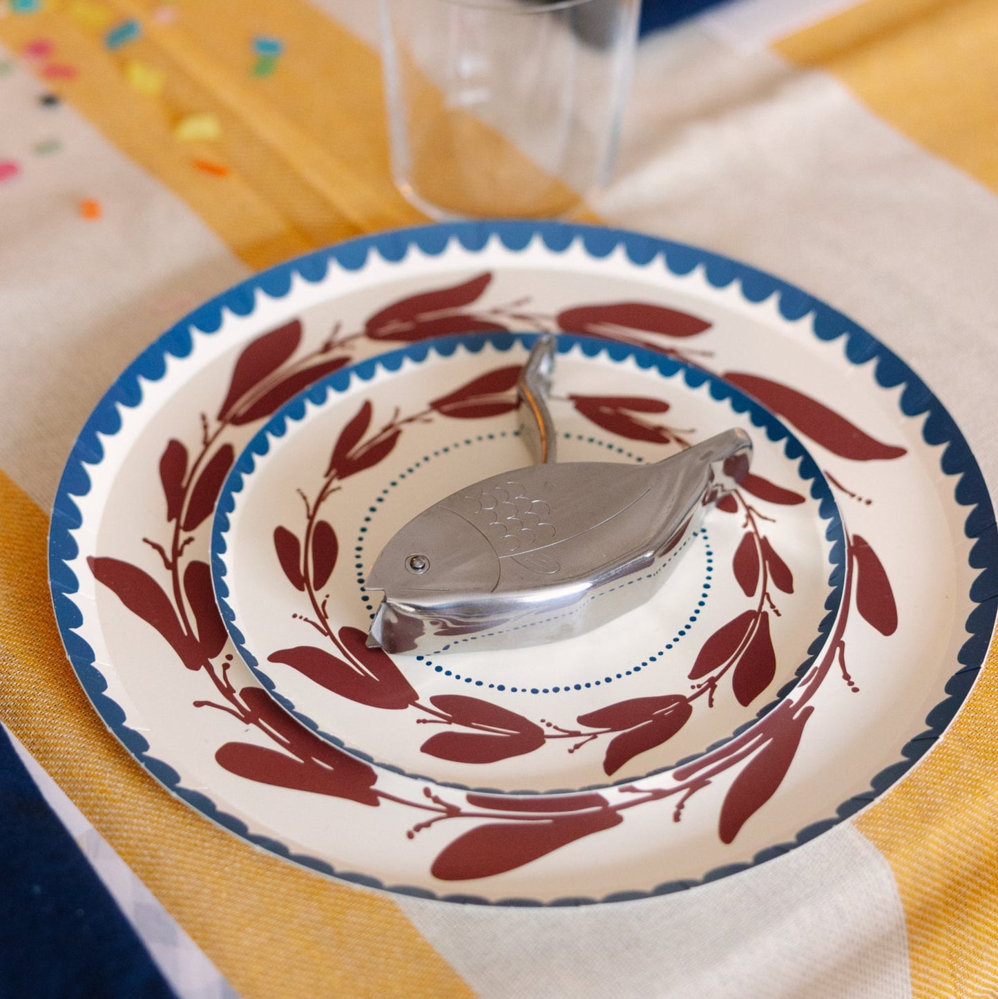 Decorative table setting with a plate, cutlery, and glass on a yellow and white checkered tablecloth.