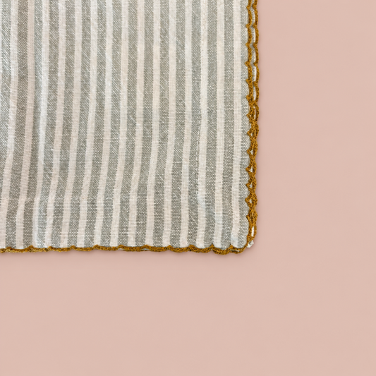 Close-up of striped cotton napkin with scalloped edge on blush background