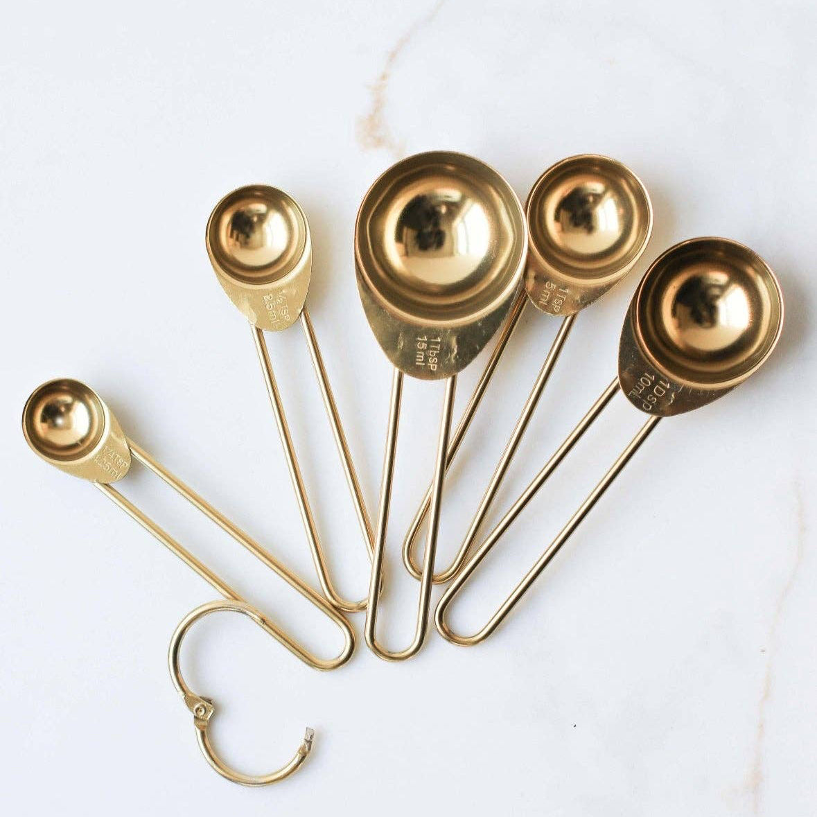 Set of gold measuring spoons on a white marble surface