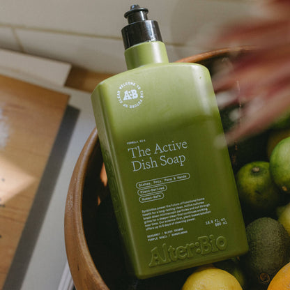 Green bottle of 'The Active Dish Soap' by Alter-Bio on a wooden surface with fruits.