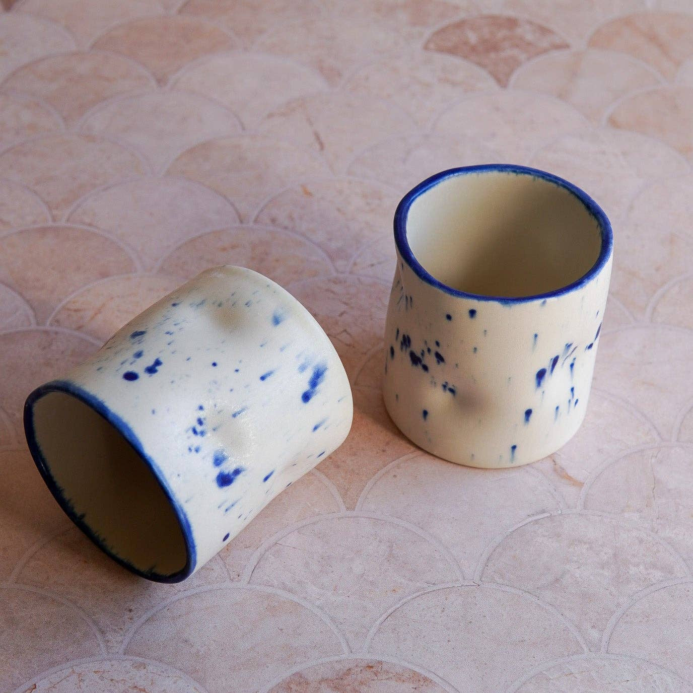 Two ceramic cups with blue rims on a textured surface