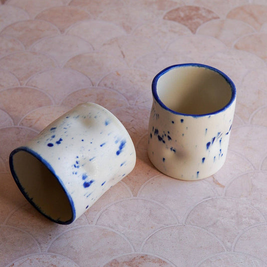 Two ceramic cups with blue rims on a textured surface