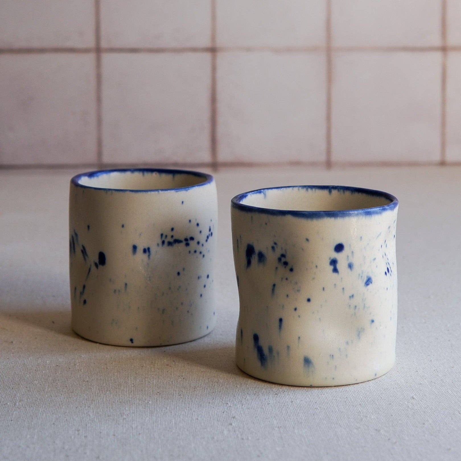 Two ceramic cups with blue speckles on a neutral background