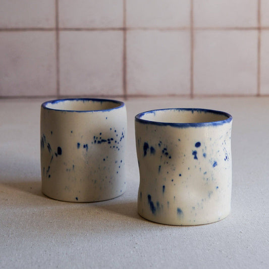 Two ceramic cups with blue speckles on a neutral background
