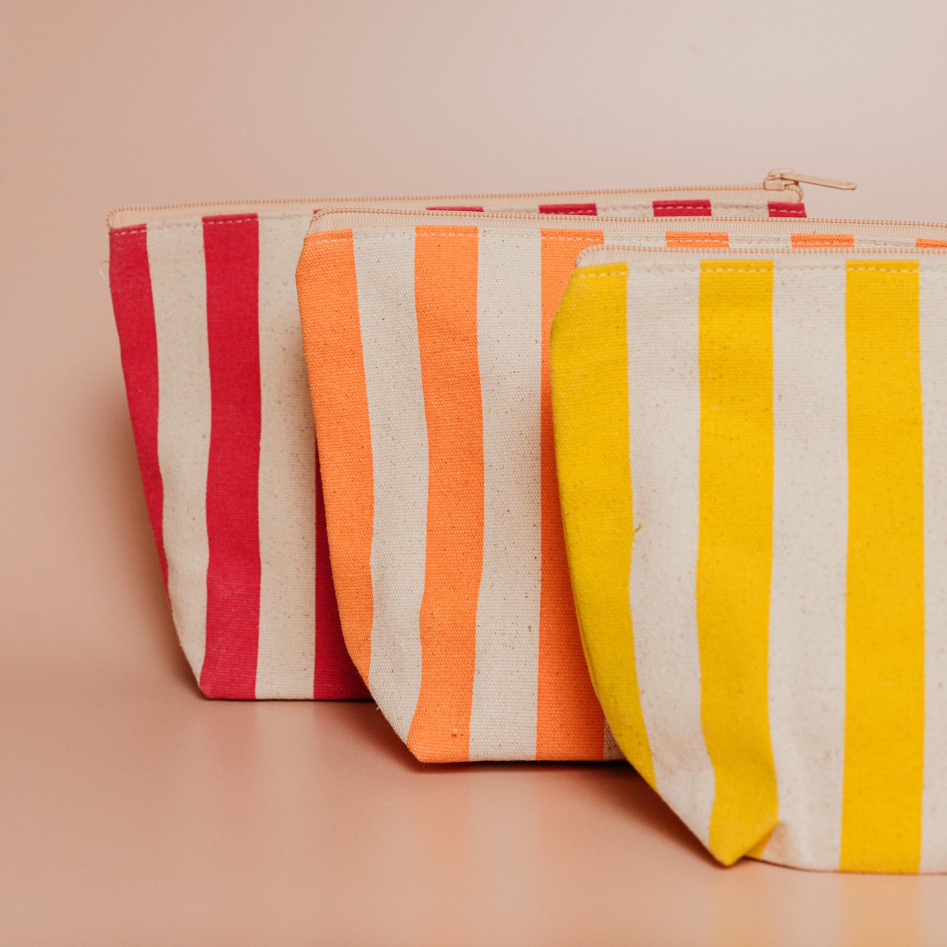 Three striped pouches in red, orange, and yellow on a beige background