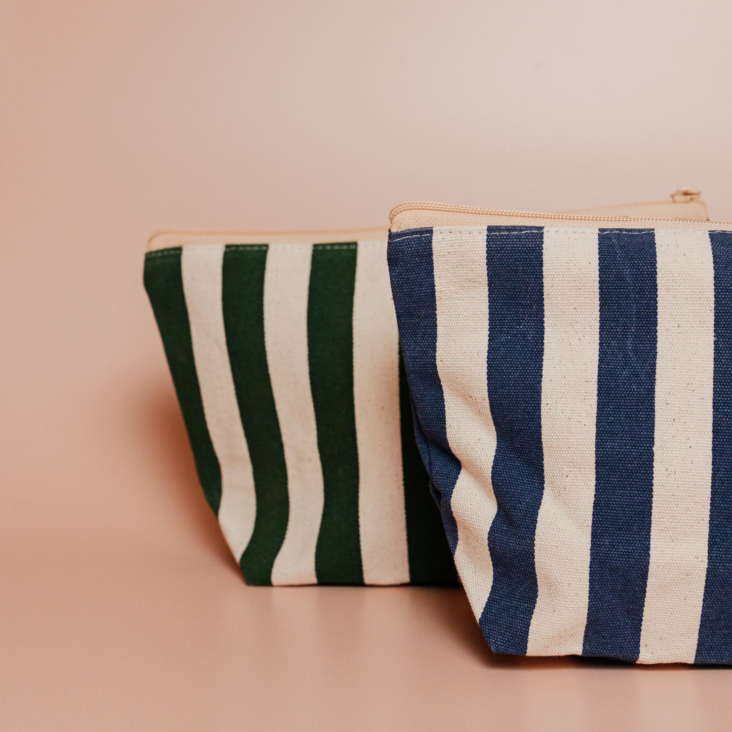 Two striped pouches, one green and beige, the other blue and beige, on a pink background.