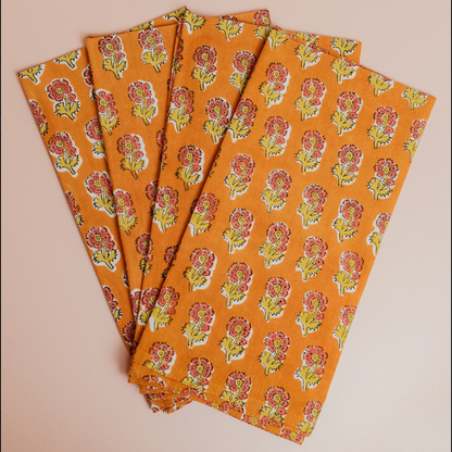 Set of four orange fabric napkins with floral pattern on a beige background
