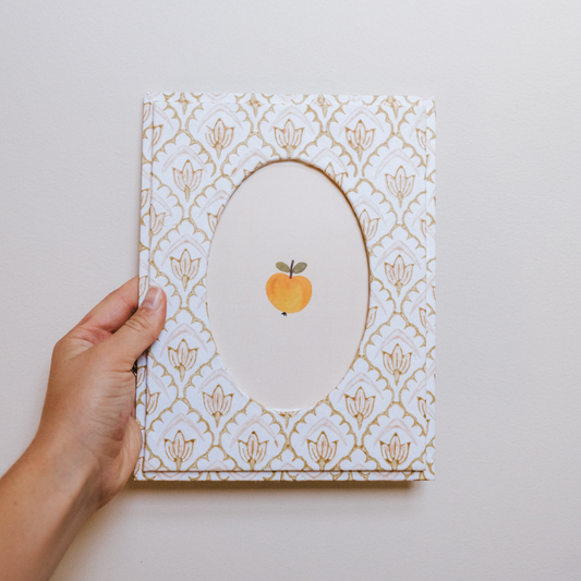 Hand holding a card with a decorative pattern and an orange fruit illustration on a light gray background