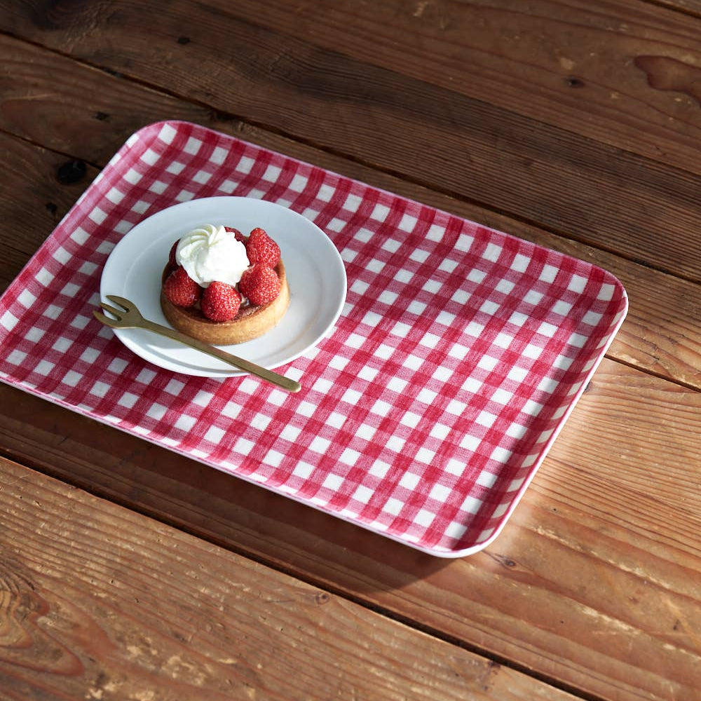 A red and white checkered tray liner placed on a wooden surface, with a plate and a dessert on top of it.