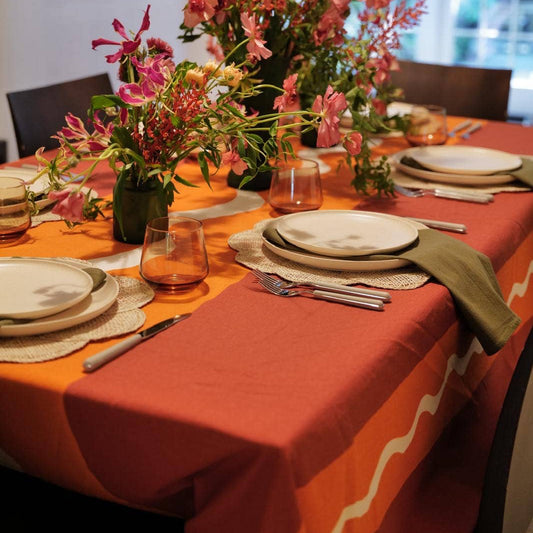 Dining table set with an orange tablecloth, floral centerpiece, and white plates.