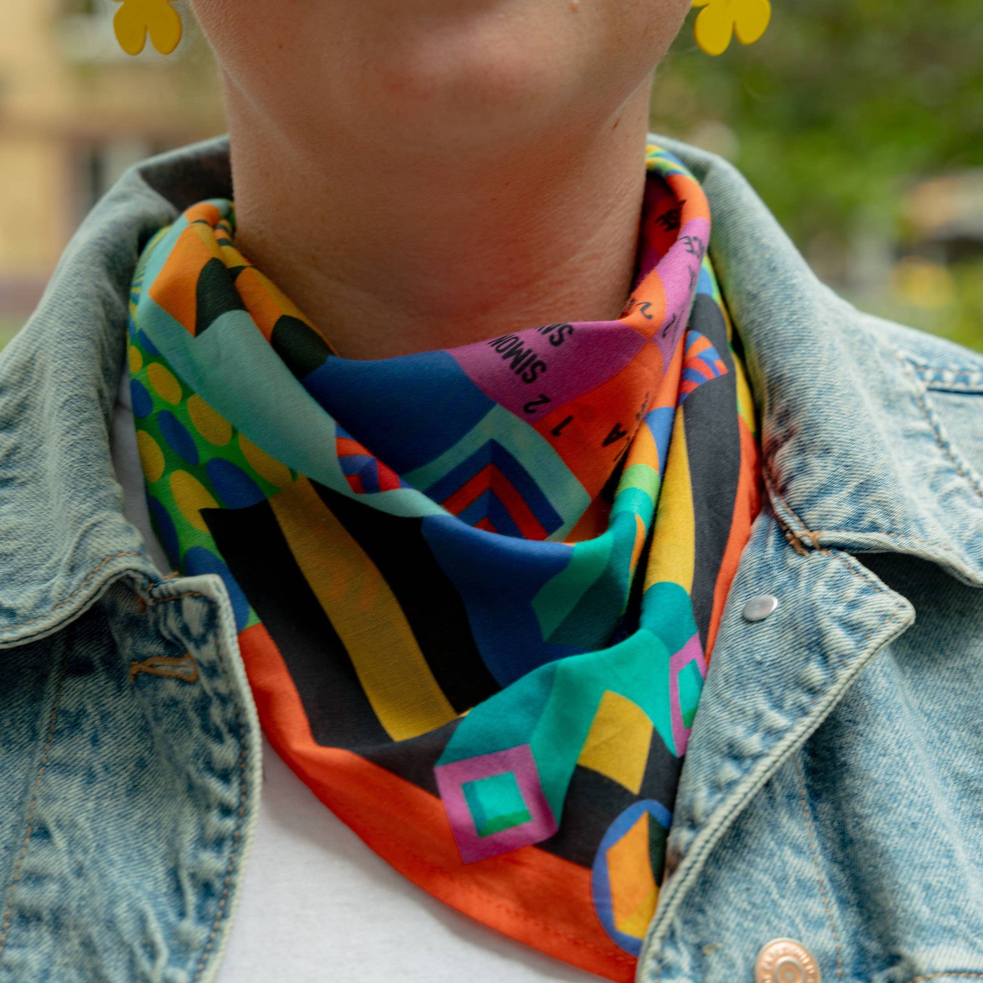 Person wearing a colorful scarf and denim jacket with a blurred outdoor background