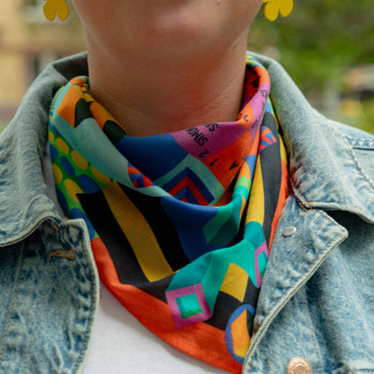 Person wearing a colorful scarf and denim jacket with a blurred outdoor background