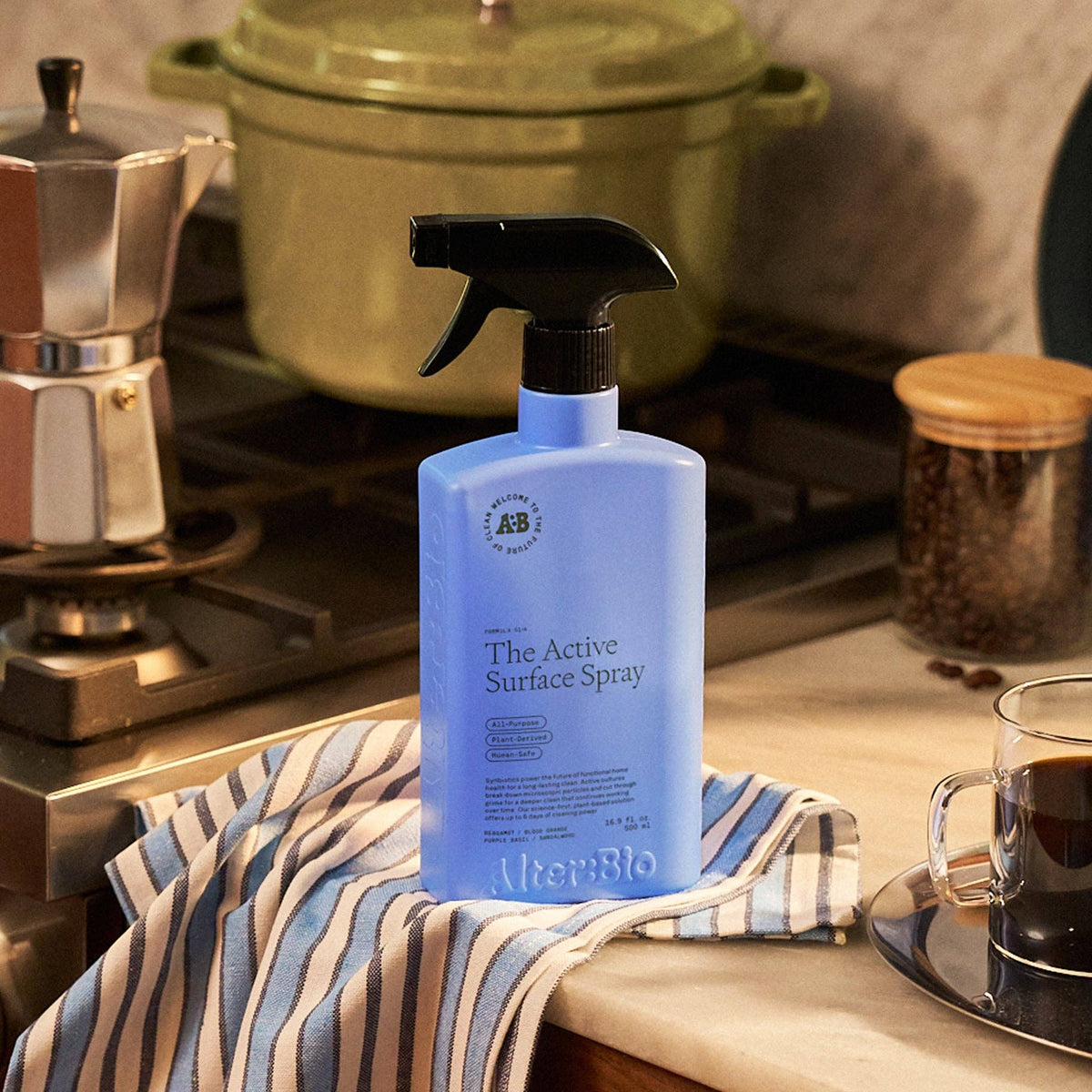 Blue bottle of surface spray on a kitchen counter with a striped towel and coffee cup.
