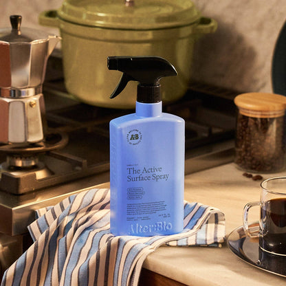 Blue bottle of surface spray on a kitchen counter with a striped towel and coffee cup.