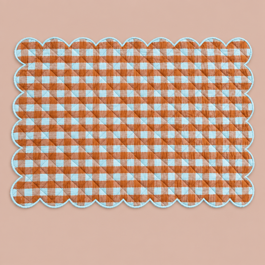 Scalloped brown and blue gingham placemat without tableware on blush background