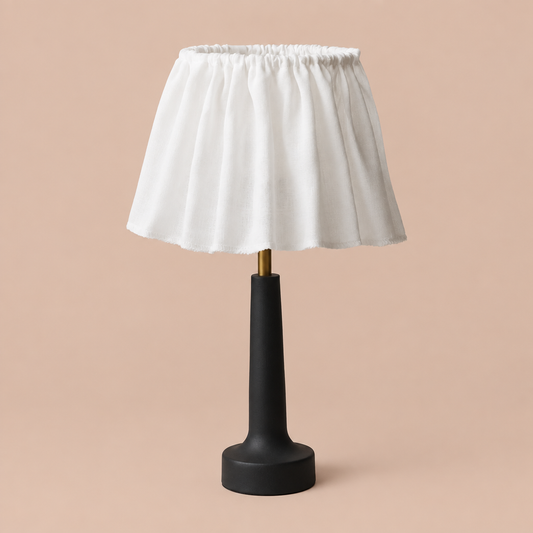 Voltaire petite table lamp with white ruffled shade, black base, and brass stem on a neutral background