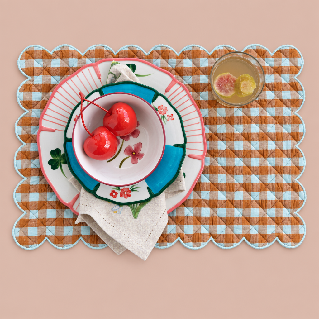 Scalloped brown and blue gingham placemat styled with tableware on blush background