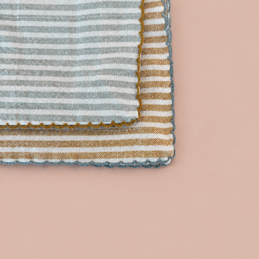 Close-up of two striped scalloped cotton napkins on blush background