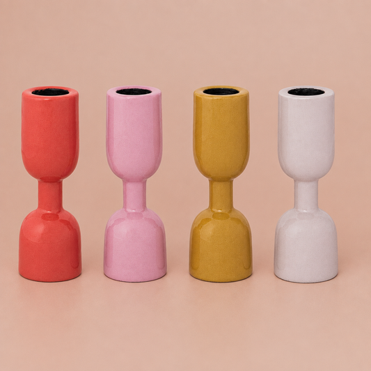 Four colorful enamel taper holders on a warm blush background